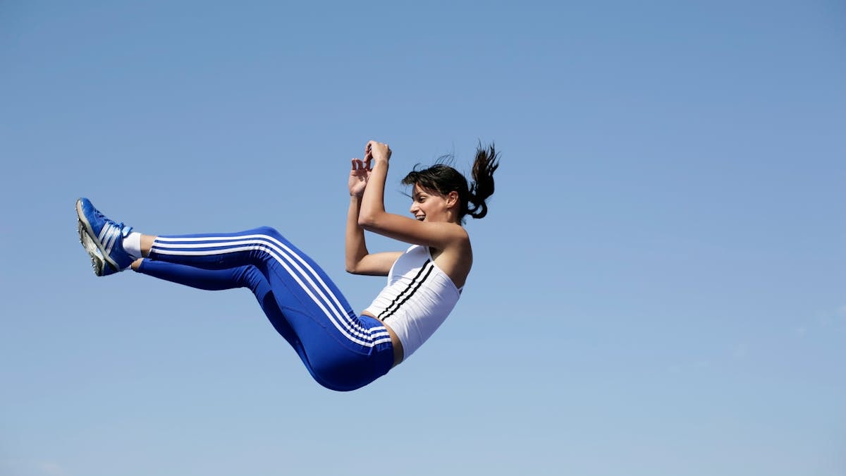 A woman in blue sportswear jumps energetically against a clear sky.